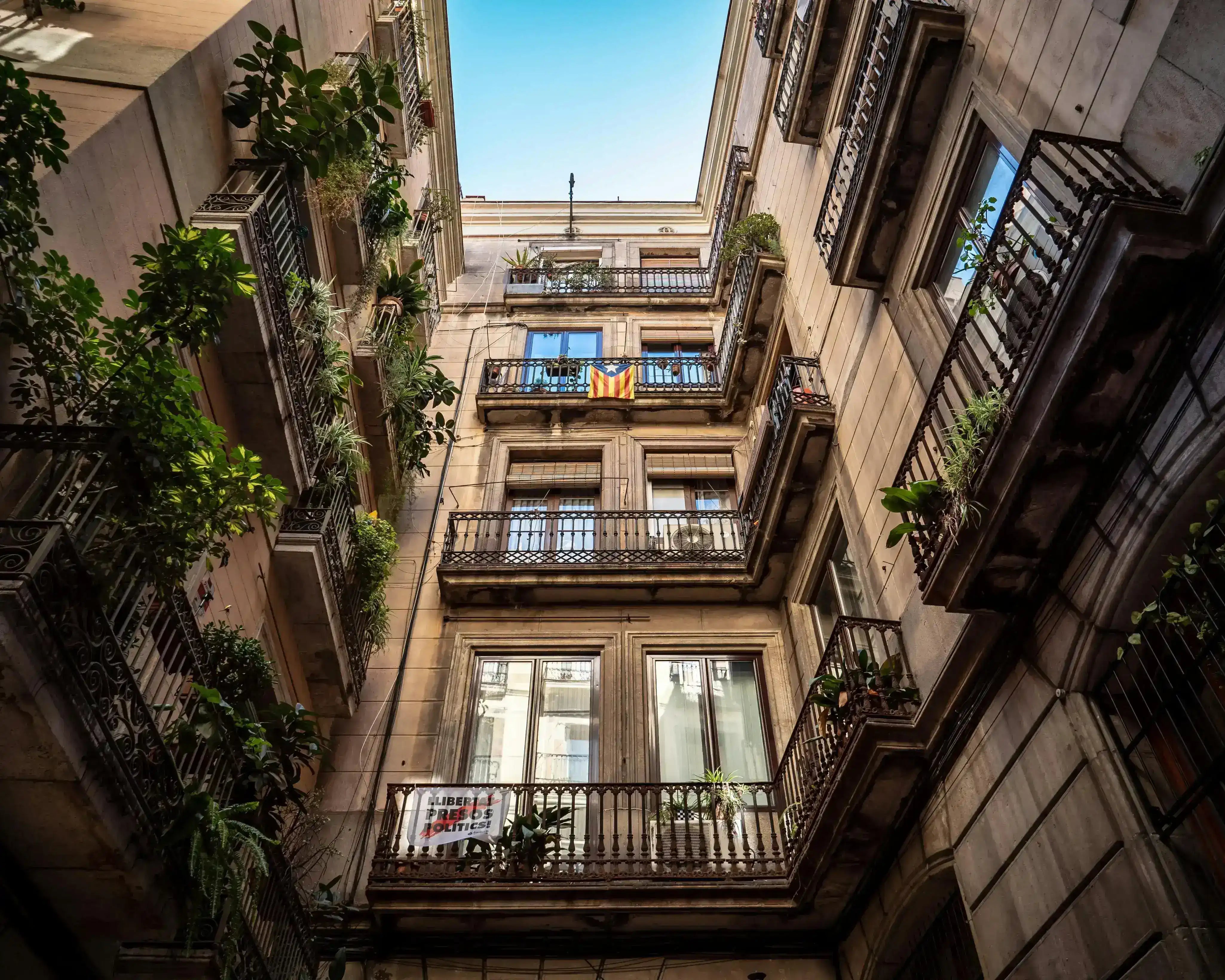 Utsikt över en innergård med balkonger i en gammal byggnad. En balkong pryds av en katalansk flagga.