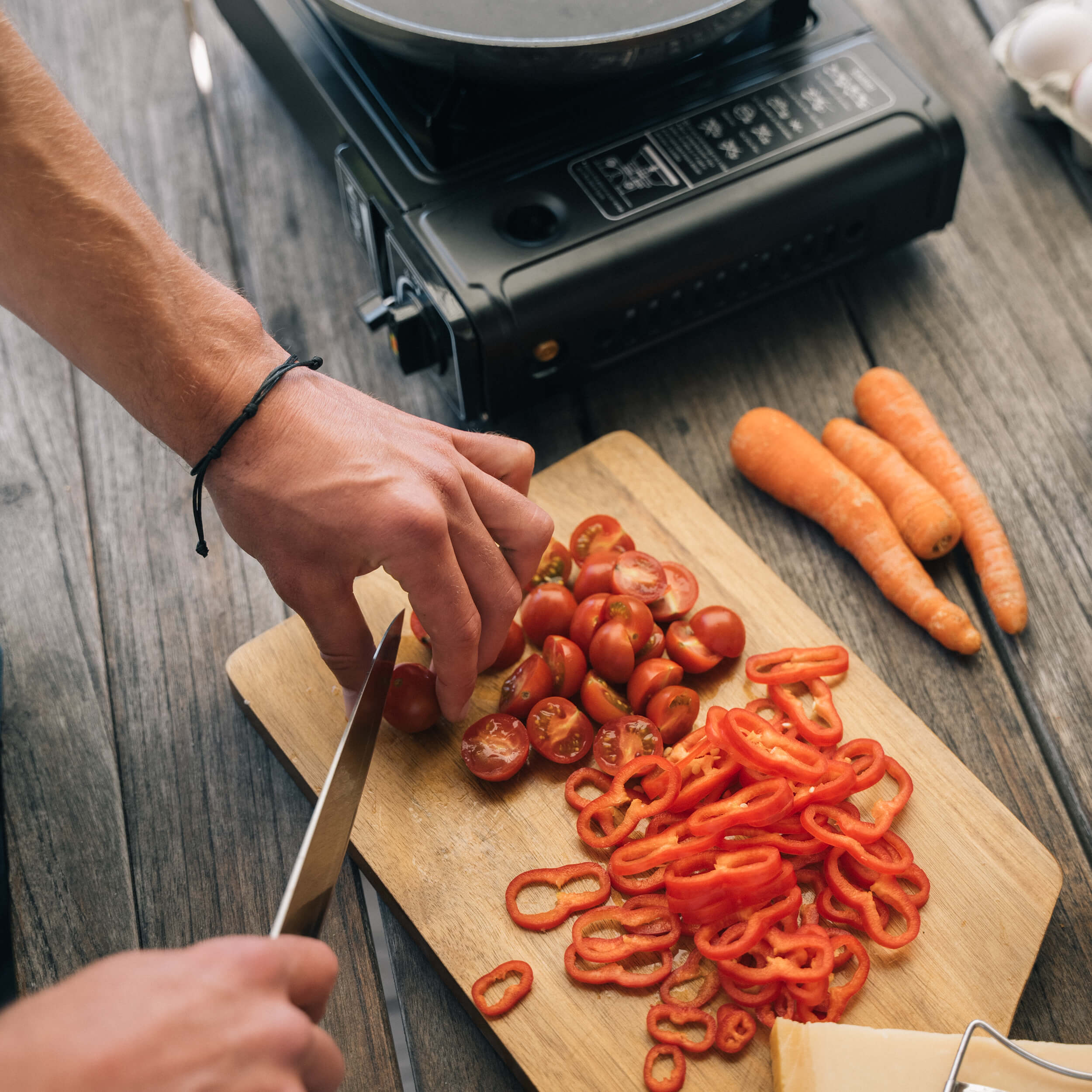 En person hackar tomater och röd paprika på en skärbräda, med ett gasolkök i bakgrunden.