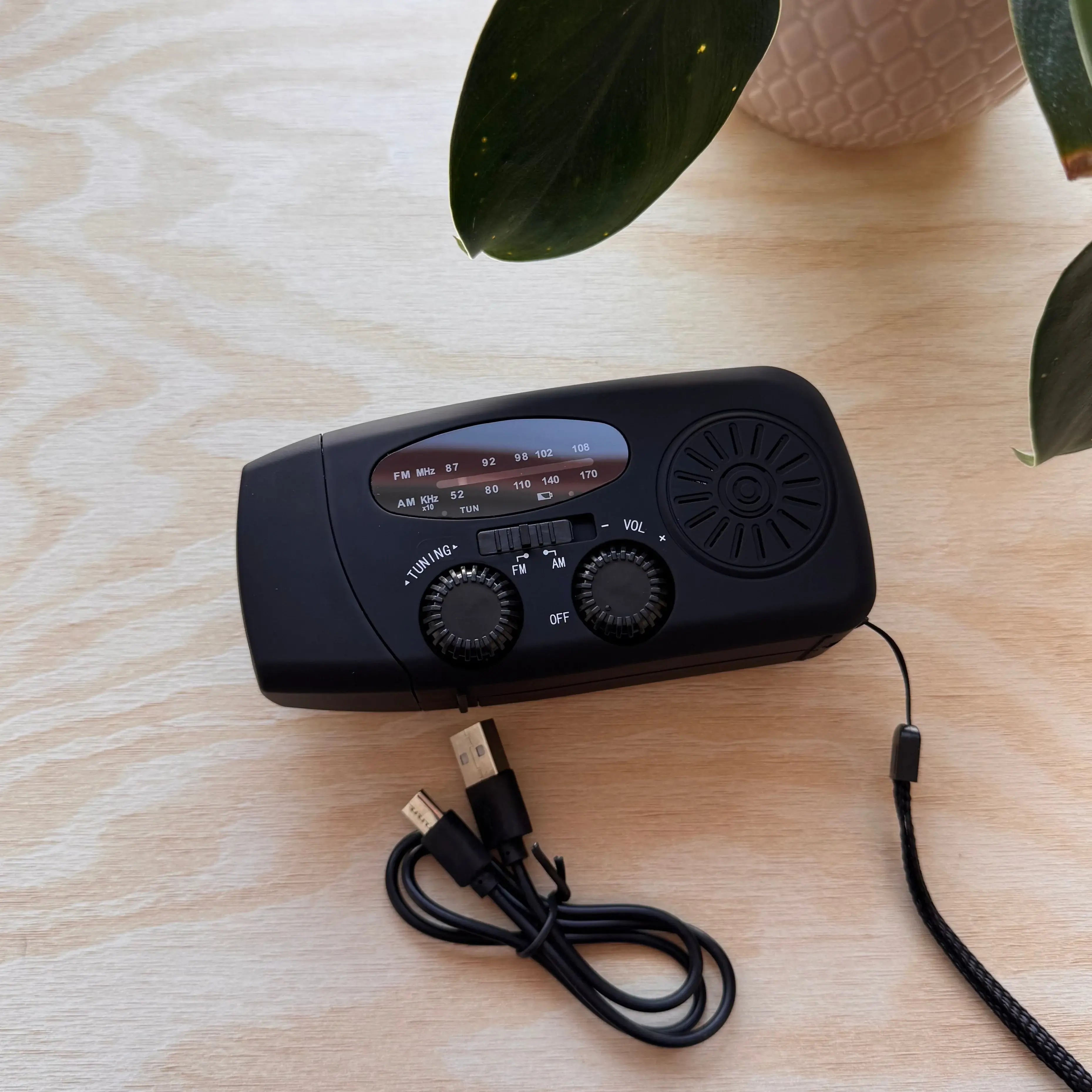 En svart vevradio med synliga rattar för inställning och volym, samt en laddkabel.