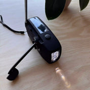 En svart vevradio med solpanel och ficklampa, med ett utfällt vevhandtag.