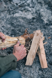 En person snitter et stykke træ med en kniv for at forberede træ til et bål.