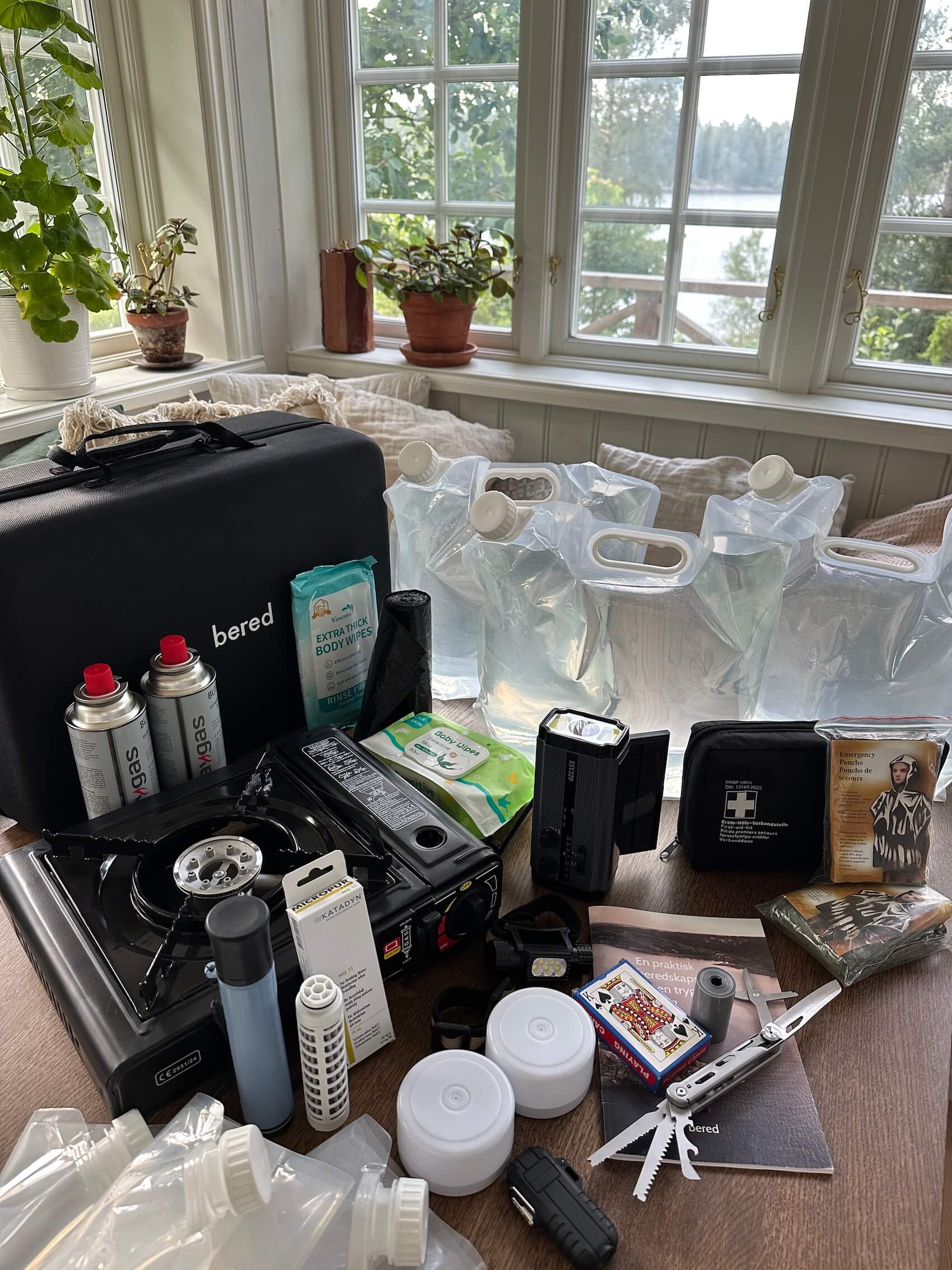 Ett stort bord fullt med hemberedskapsartiklar, inklusive vattenbehållare, gasolkök, väska och ficklampa.