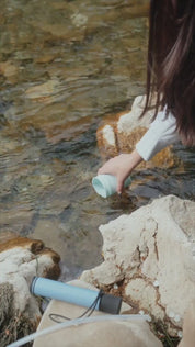 Person som fyller ett bärbart vattenfilter med vatten från en bäck.