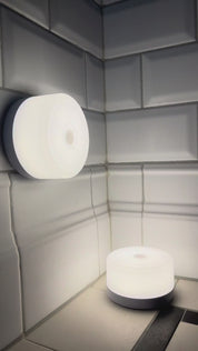 Två runda, batteridrivna lampor som lyser i ett hörn med vita kakelplattor.