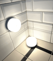 Två runda, batteridrivna lampor som lyser i ett hörn med vita kakelplattor.