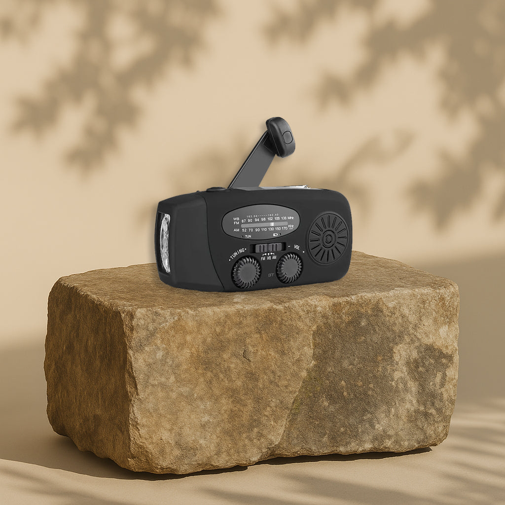 En sort håndsvingradio med solpanel og lommelygte, placeret på en kampesten med skygger i baggrunden.