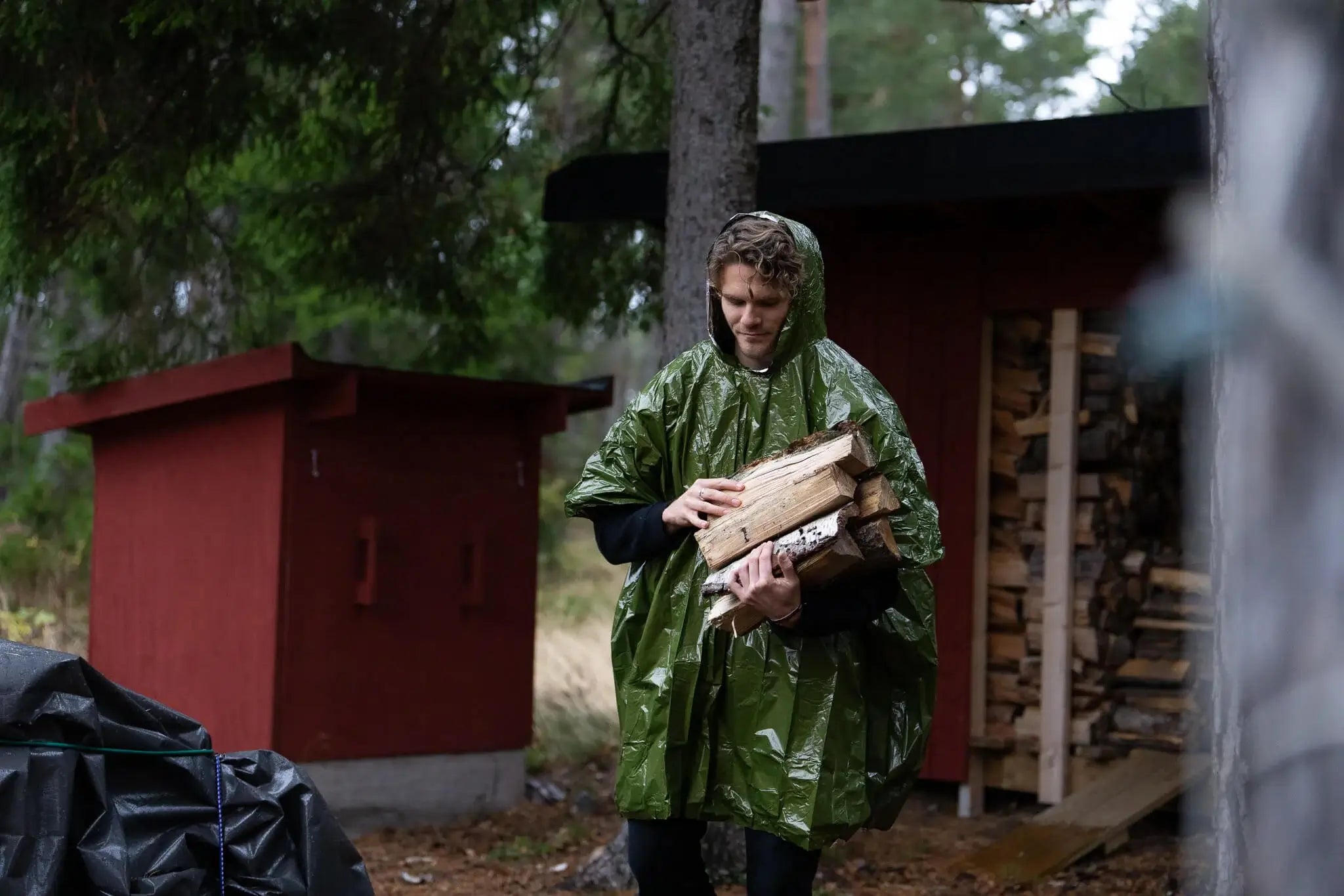 Test av krisberedskapsutrustning i verkligt scenario utomhus – person i regnponcho bär ved vid dåligt väder som del av praktiskt stresstest