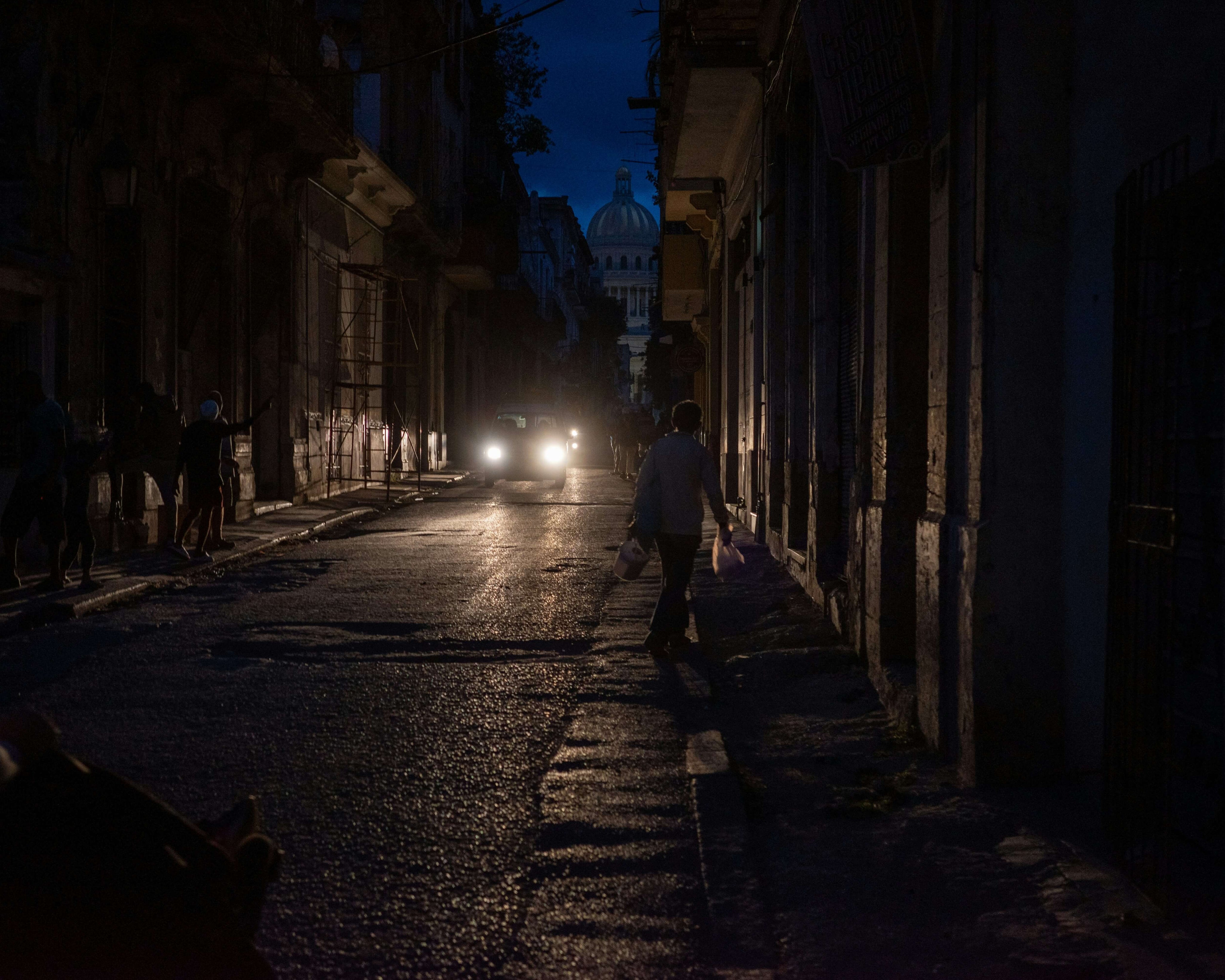 Mörk svensk stadsgata under kvällstid med begränsad belysning, där silhuetter rör sig i låg ljusnivå och strålkastare bryter mörkret – illustrerar behovet av tillförlitlig information och rutiner vid elavbrott.