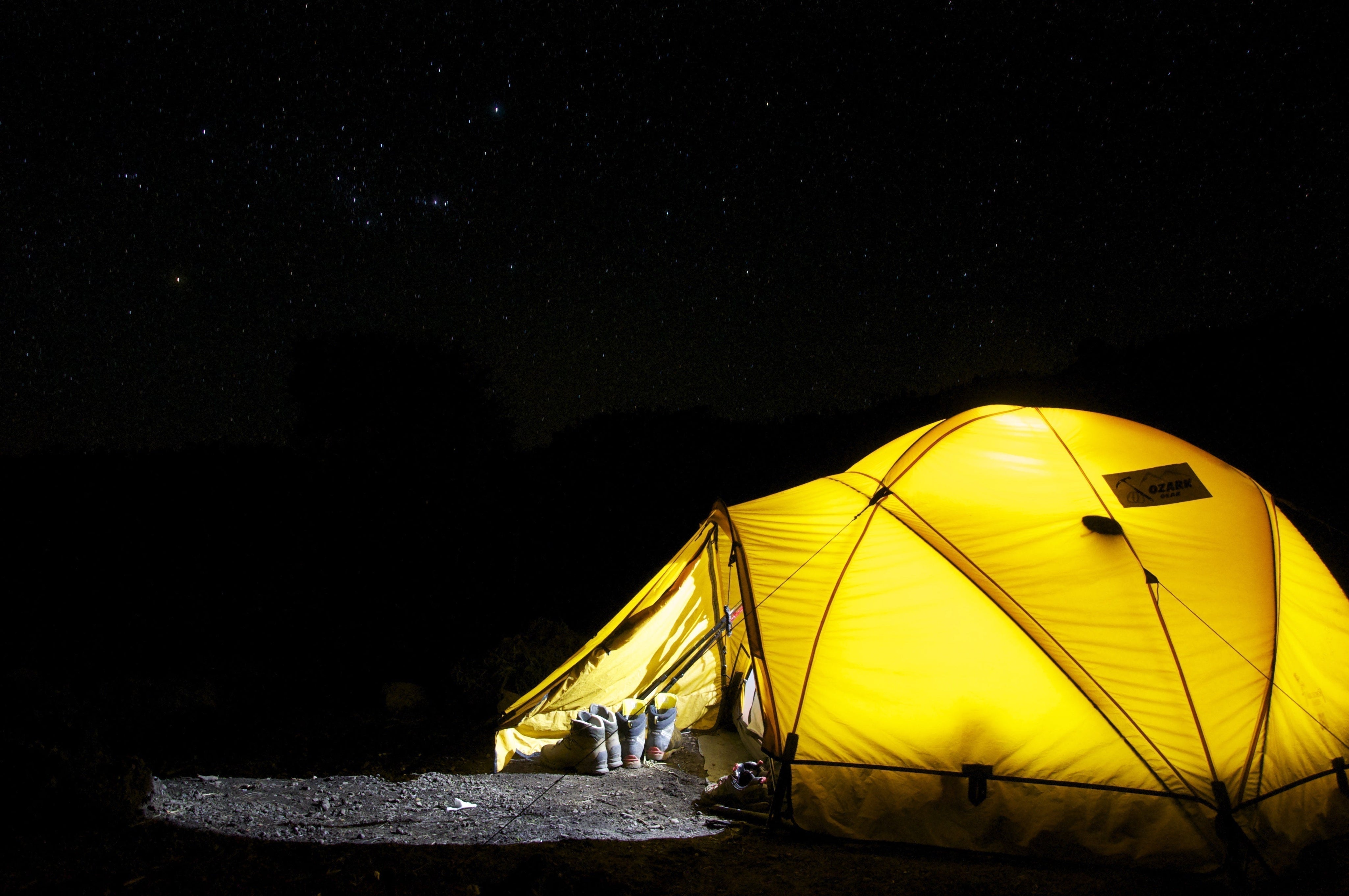 Upplyst gult tält i mörker under stjärnhimmel, off grid-camping