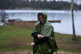 En person i nödponcho med huva står vid en sjö i regnigt väder