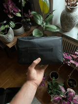 En hand håller en liten svart väska med ett handtag i bakgrunden.