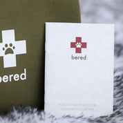 En vit broschyr för ett "bered" första hjälpen-kit för hundar och katter ligger bredvid en grön väska.