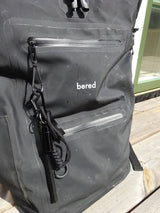 En svart, vattentät ryggsäck med "bered" logotyp, har en tändstål fäst vid en dragkedja.