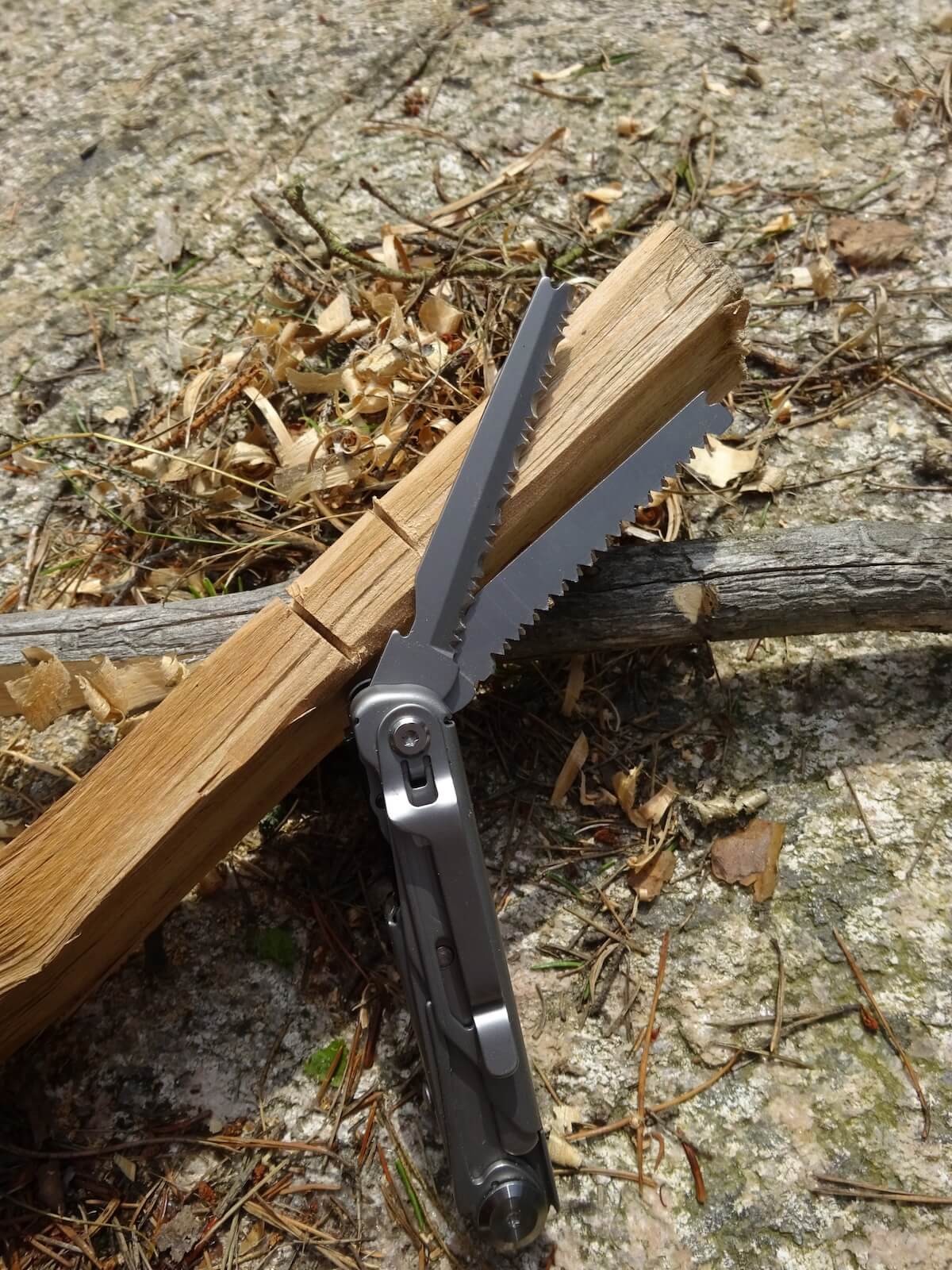 En såg från ett multiverktyg sågar i en träbit, med sågspån på marken.